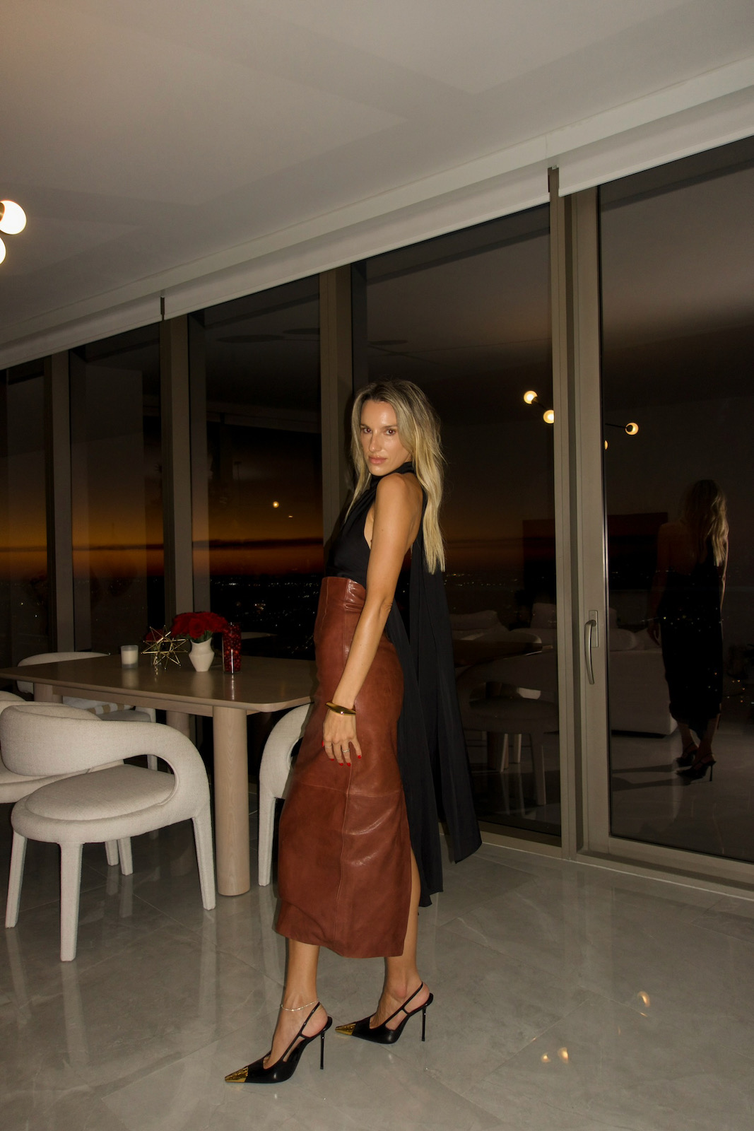Woman in a chic evening outfit featuring a brown leather skirt, black sleeveless top, and classic black heels.