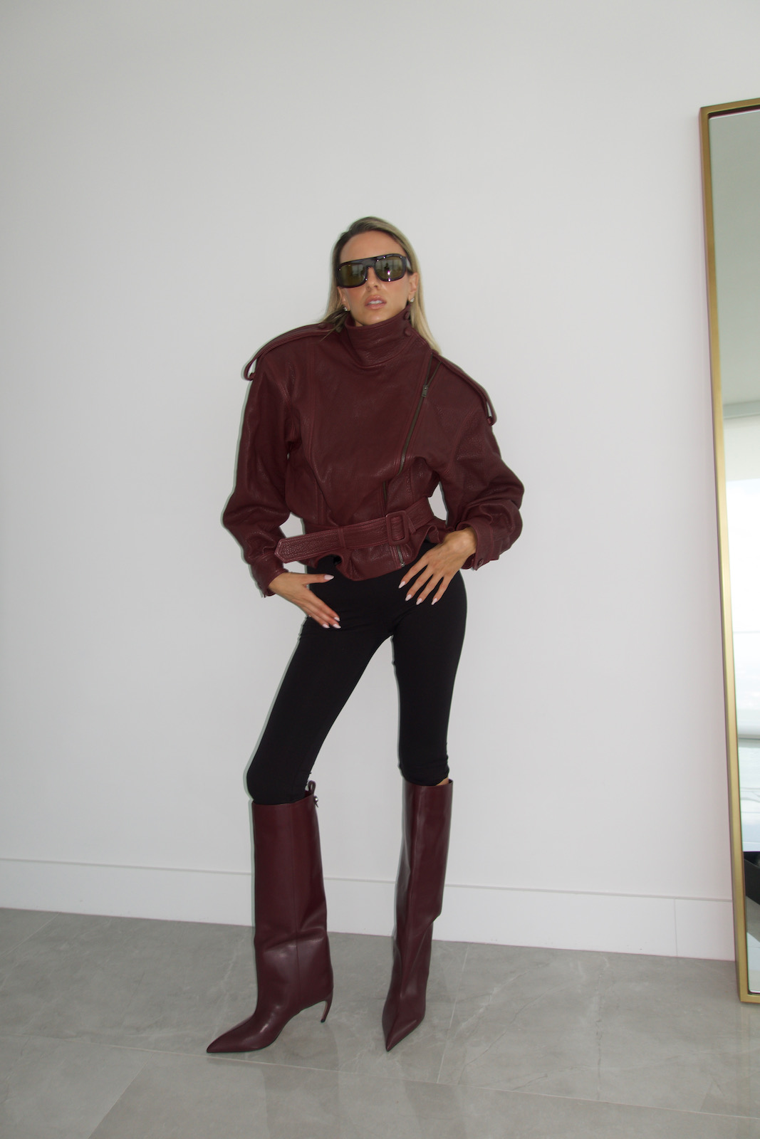 Full-length look featuring a burgundy leather jacket, black leggings, and pointed-toe knee-high boots for a sleek modern outfit